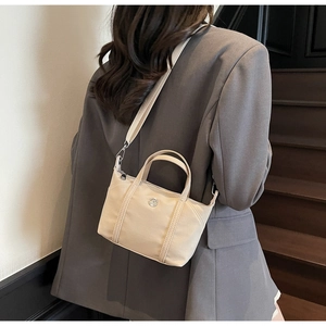 Woman in grey suit carrying a cream canvas crossbody bag on a wooden staircase