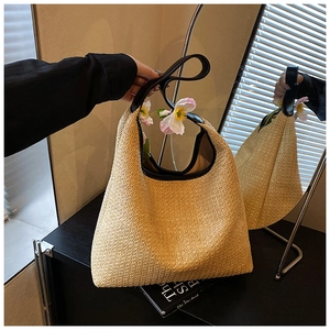 Detail of beige woven straw tote bag with black leather handles and embossed text branding