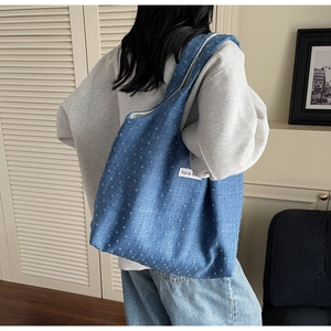 Detail of blue canvas tote bag with white polka dot jacquard pattern and woven side label