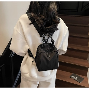 Rear view of a black nylon mini backpack with woven handles on a model by stairs
