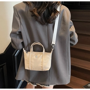 Detail of a beige canvas mini tote bag with a metallic logo on a wooden staircase