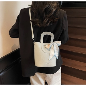 Vista posteriore di una modella con borsa a secchiello celeste a trama litchi e foulard di seta