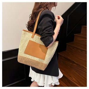 Straw tote bag with brown leather handles worn by model on stairs in a summer setting