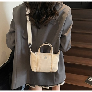 Close-up of cream canvas crossbody bag with silver metal logo and adjustable wide strap