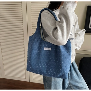 Detail of blue textured tweed tote bag with logo patch and woven dot pattern