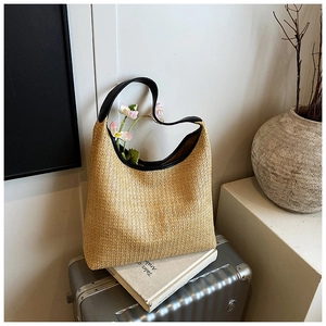 Detail of woven straw tote bag with black leather handle and embossed text on suitcase