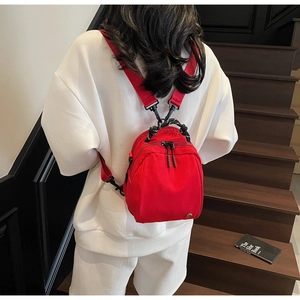 Close-up of a bright red mini backpack with black and white handle worn by a model
