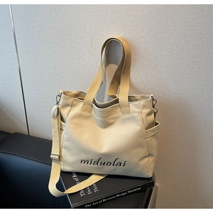 Detailed shot of beige canvas tote with long shoulder strap and brand logo on book