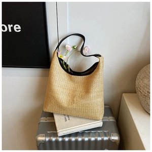 Detail of a beige woven straw bag with black leather trim and BAG lettering