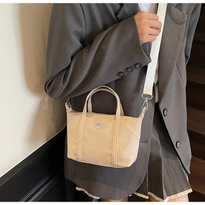 Detail shot of beige mini nylon tote bag with metal logo and adjustable shoulder strap