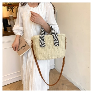 Détail du sac cabas en paille beige avec anses rayées et bandoulière sur un modèle