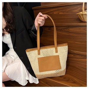 Detail of a large straw tote bag with brown leather handles on wooden stairs