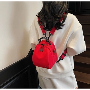 Close-up of a red waterproof nylon mini backpack worn by a model in a modern indoor setting