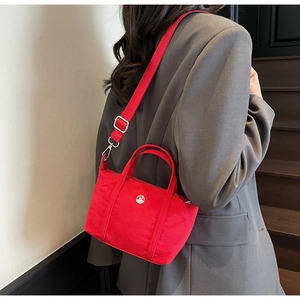 Detail of red canvas tote bag with adjustable strap worn over a grey blazer