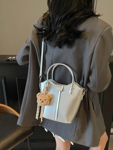 Silver metallic bucket bag with bear pendant shown in a stylish studio setting