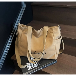 Detail view of khaki canvas tote bag with iduolai lettering and side pocket on wooden steps
