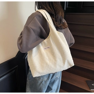 Detail of off-white tote bag showing 3D raised dot texture and brand logo label