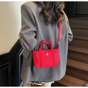 Detail of red nylon handbag with metal M logo shown against a grey blazer suit