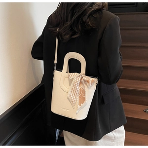 Dettaglio borsa a secchiello color crema con trama litchi e foulard di seta geometrico