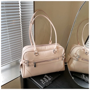 Detail of a beige Boston bag with dual long handles and decorative zippers on a black surface