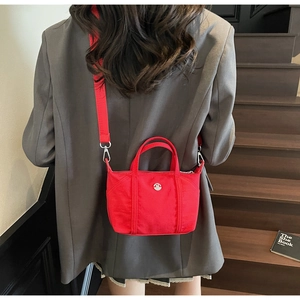 Detail of red canvas crossbody bag with adjustable wide strap and circular logo