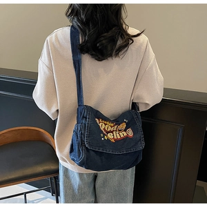Detail of blue denim crossbody bag with colorful embroidery on a back-view model