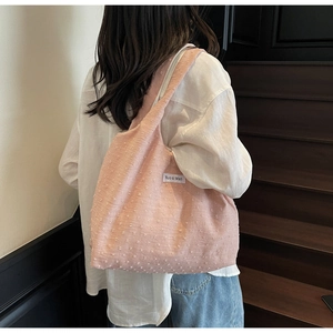Close-up of pink tote bag with textured dot fabric and brand label on shoulder