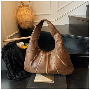 Close-up of vintage brown leather tote bag with vertical stitching on wooden stairs