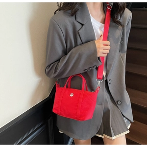 Detail of red canvas mini tote bag with metal buckle on a grey suit outfit background