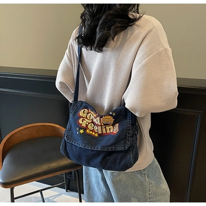 Detail of vintage blue denim messenger bag featuring colorful Good Feeling embroidery