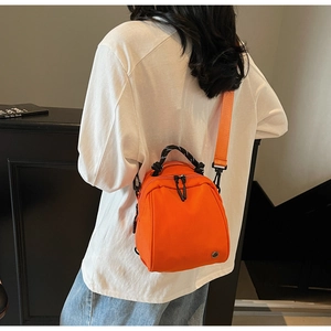 Rear view of model wearing a bright orange nylon shell bag with woven handle