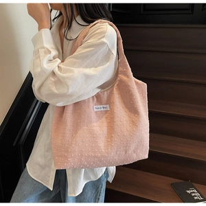 Pink canvas tote bag with textured dots and branded label worn by a model in a lifestyle setting