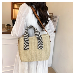 Détail du sac cabas en paille avec poignée rayée et bandoulière en cuir marron au café