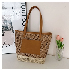 Close-up of woven straw tote bag with brown leather pocket and dual handles detail