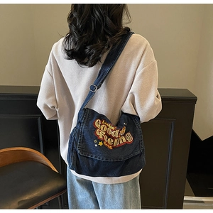 Detail of vintage denim crossbody bag featuring textured embroidery and adjustable strap