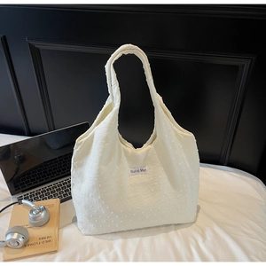 Close-up of white quilted tote bag with textured dots and branded woven label