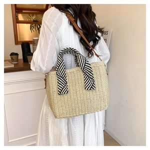 Détail du cabas en paille avec poignées rayées et bandoulière en cuir réglable pour femme