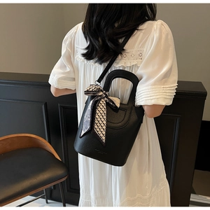Dettaglio della borsa a secchiello nera in pelle martellata con foulard di seta geometrico