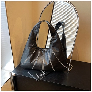 Close-up of black vintage leather hobo bag with contrast silver stitching on a dark surface