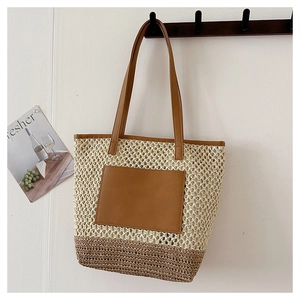 Detail view of woven straw tote bag with brown leather handles and contrast pocket