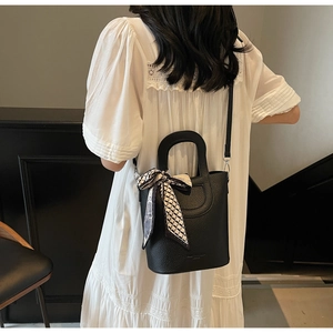 Dettaglio borsa a secchiello nera in pelle martellata con foulard decorativo in seta a scacchi