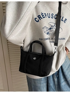 Minimalist black canvas tote bag with metal logo and adjustable crossbody strap shown on model