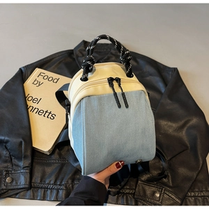 Detail of blue denim and beige faux leather backpack with woven rope handle and black zippers