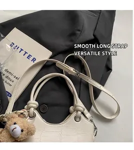 Detail of cream crossbody bucket bag with crocodile texture and brown plush bear charm