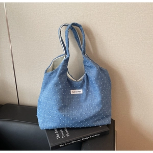 Detail of blue denim tote bag with white embroidery on a black sofa over a book