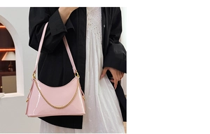 Close-up of pink patent leather bucket bag with gold chain on model in minimalist setting