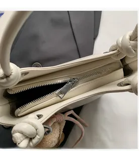 Detailed macro view of a smooth metal zipper on a minimalist cream-white shoulder bag
