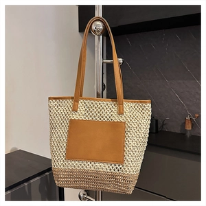 Detail of handwoven straw tote bag with brown faux leather patch and handles