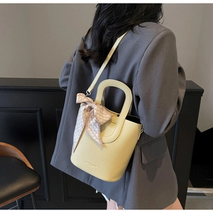 Dettaglio della borsa a secchiello gialla in pelle litchi con manico e foulard decorativo