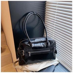 Detail of high-gloss black bowling bag featuring side decorative buckles and metal zippers